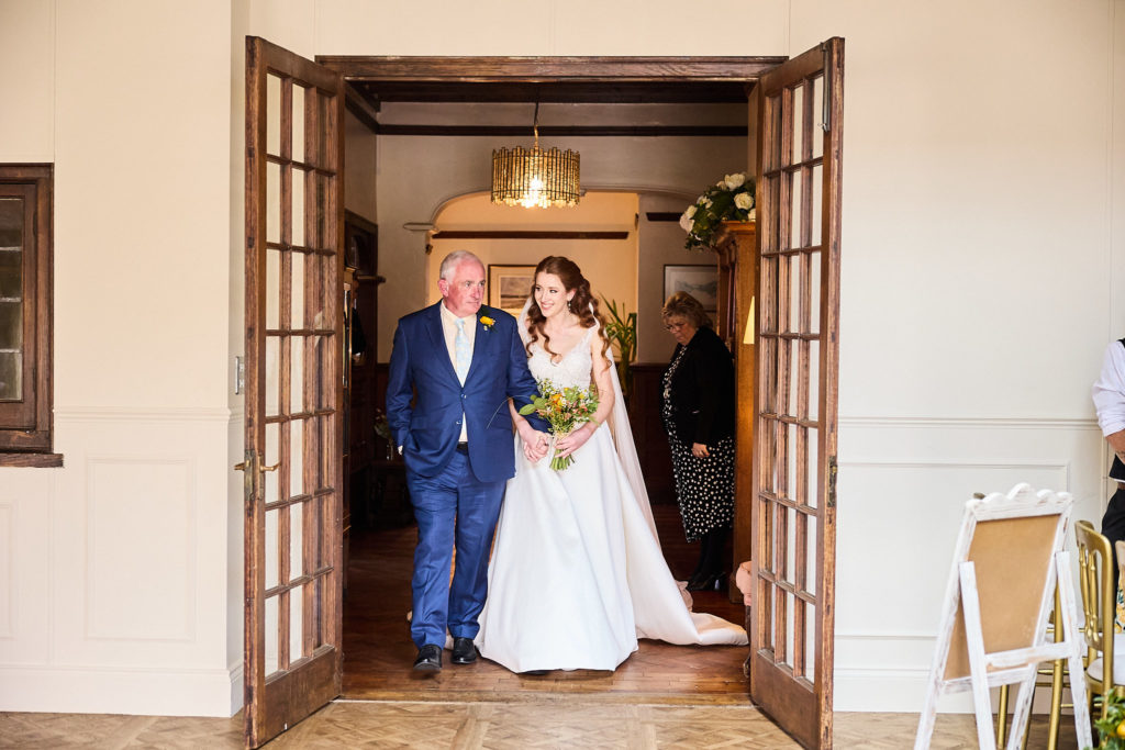 Bride and an older man in a navy suit standing in the doorway before the ceremony
