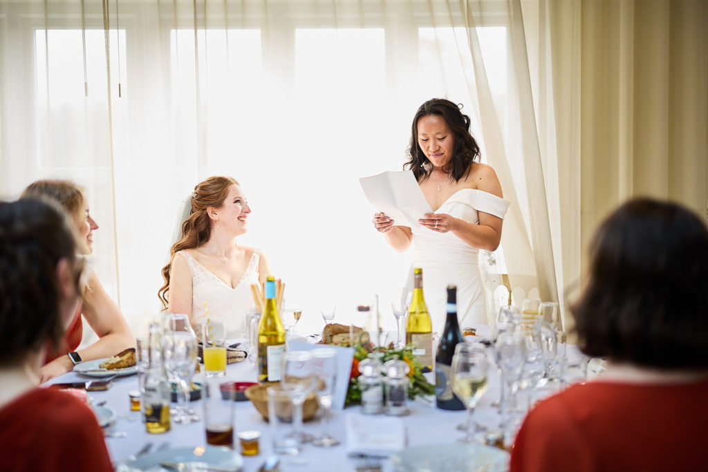 Bride giving her speech as her wife laughs beside her