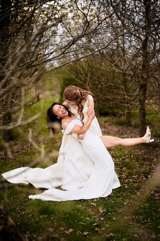 Bride dipping her wife for a kiss in the woods at Prested Hall