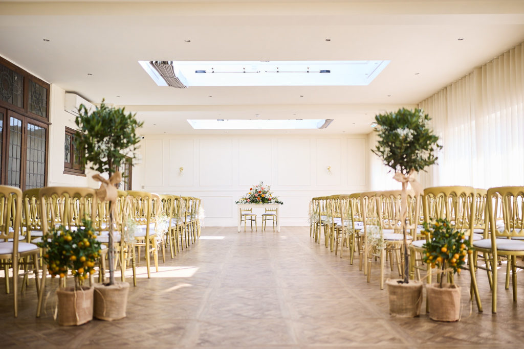 Ceremony room with gold chairs and potted olive trees at Prested Hall