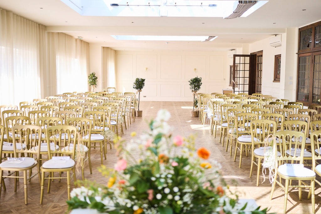 Rows of gold ceremony chairs with flowers in the foreground
