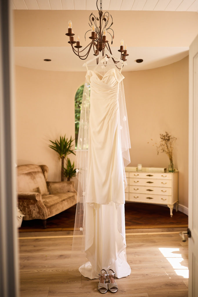 Wedding dress and veil hanging from a chandelier with bridal shoes beneath