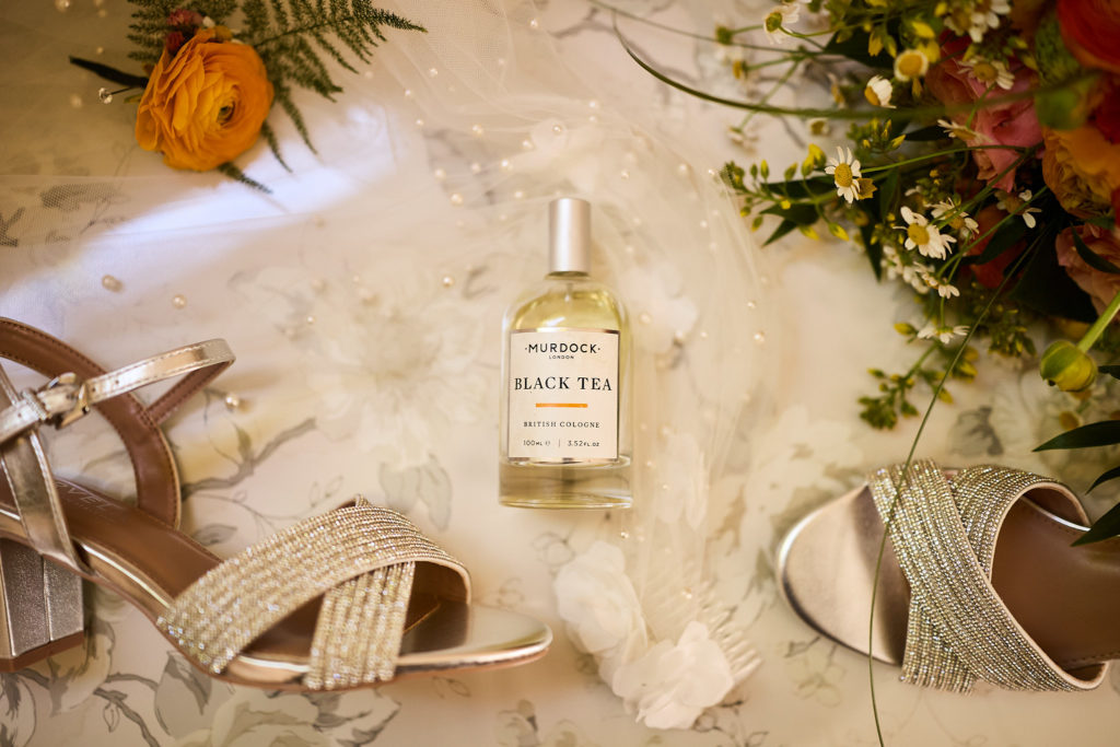 Bridal shoes and a bottle of perfume laid out with flowers