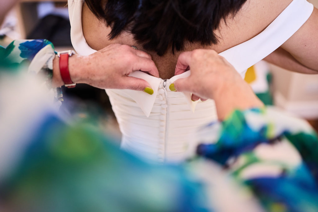 Close-up of hands fastening the back of a bride's dress