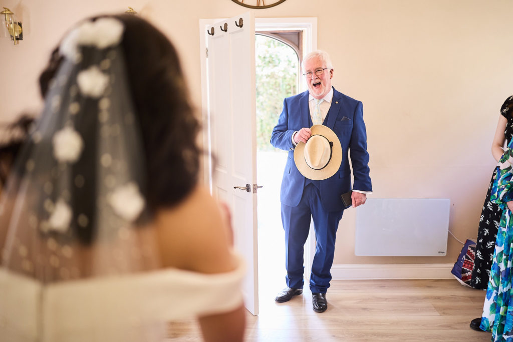 Older man in a navy suit holding his hat as he sees the bride in her dress