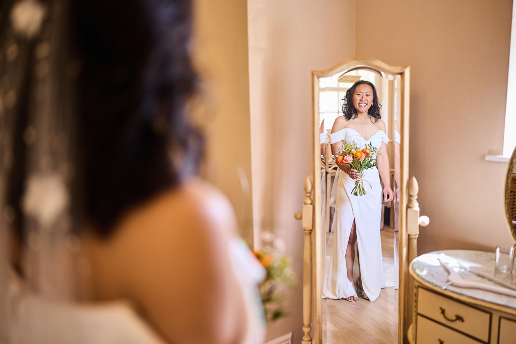 Bride reflected in a full-length mirror in her wedding dress, holding her bouquet