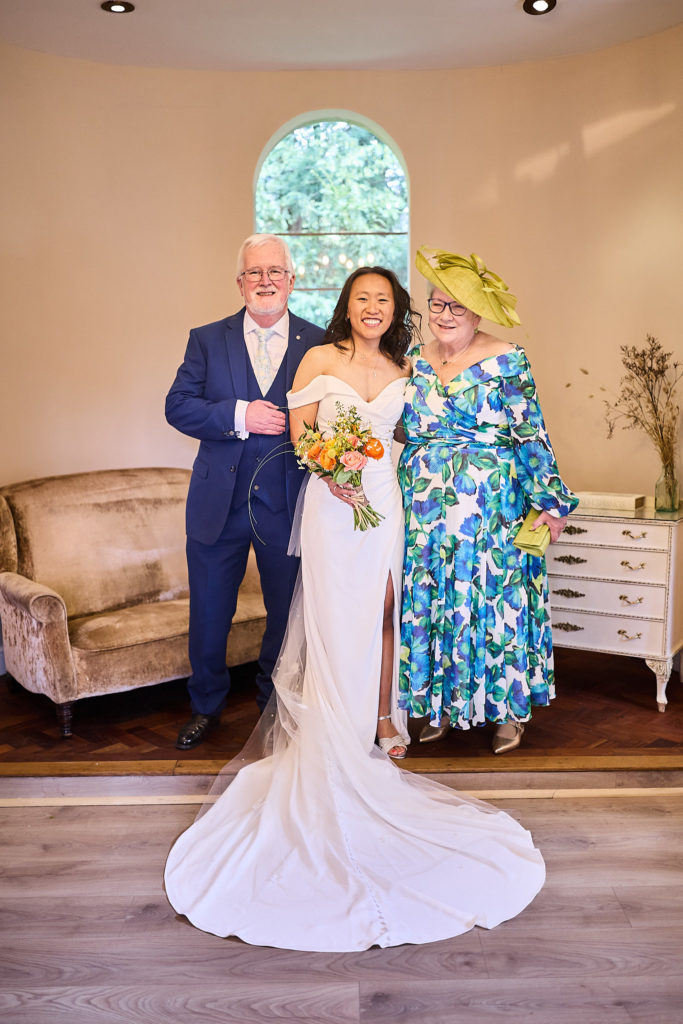 Bride standing between an older couple before the ceremony, her dress train spread out