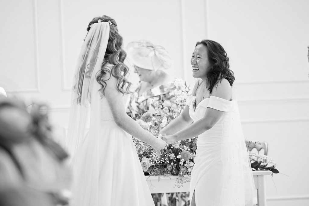 Black and white photo of the two brides holding hands across a table of flowers