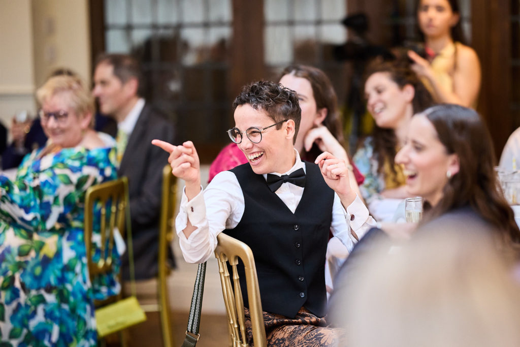 Wedding guest in a waistcoat and bow tie pointing and laughing at the table