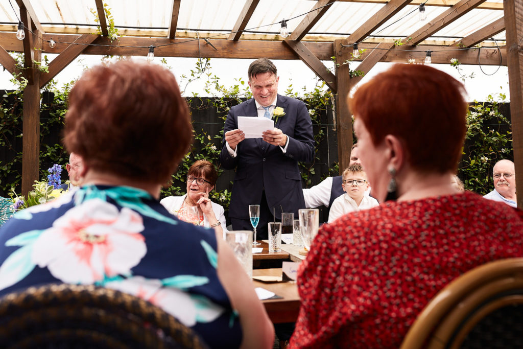 Groom giving his speech, seen between two guests at the table
