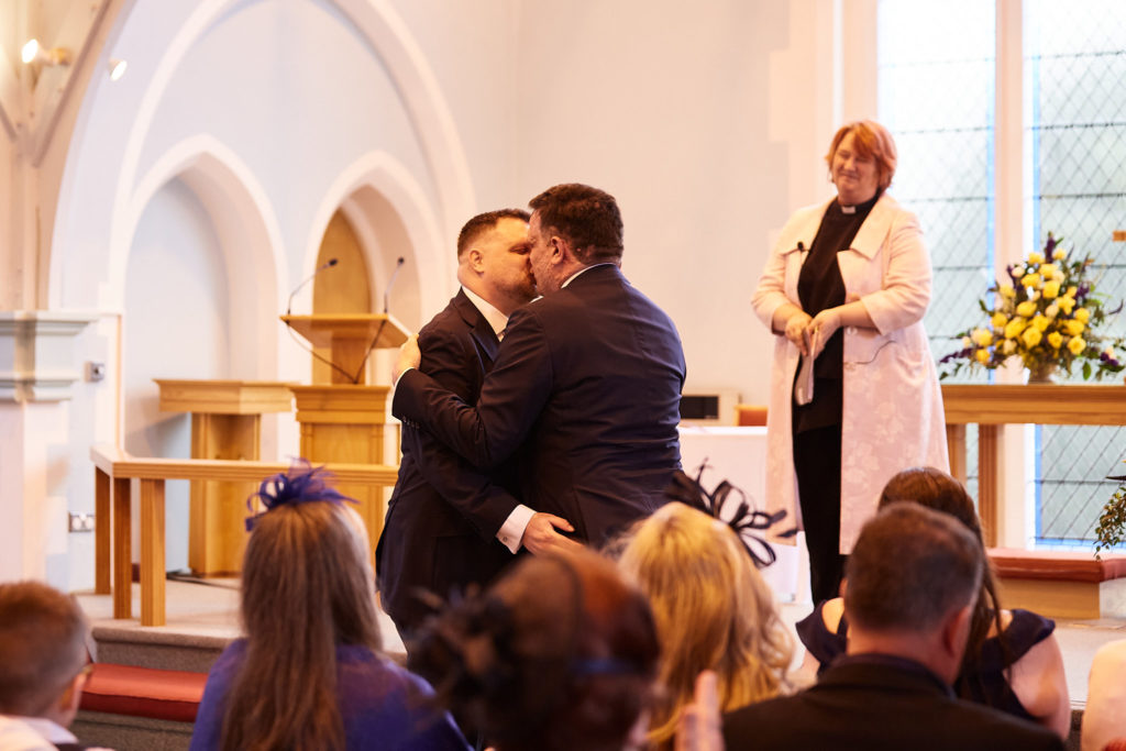 Two grooms sharing their first kiss as the minister looks on at their gay wedding in Windsor