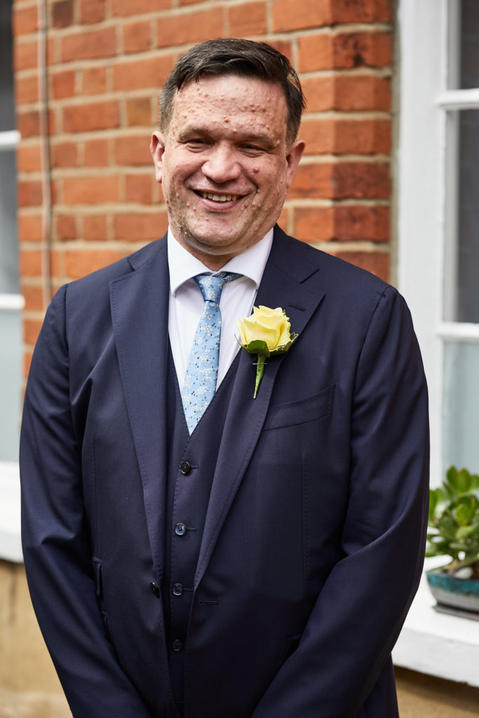 Groom laughing in a navy three-piece suit with a yellow rose buttonhole