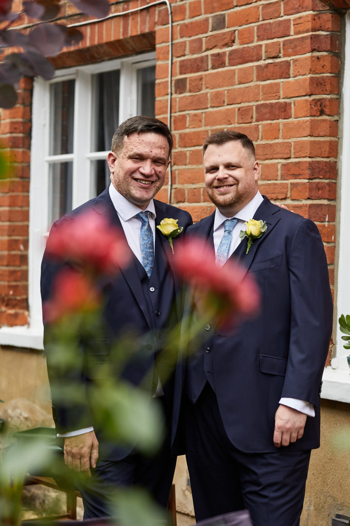 Two grooms in matching navy suits smiling together on their LGBT wedding day in Windsor