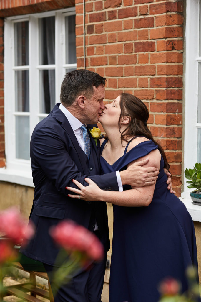Groom kissing his best woman on the cheek outside a red-brick building