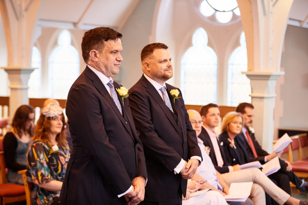Two grooms standing side by side at the front of the church