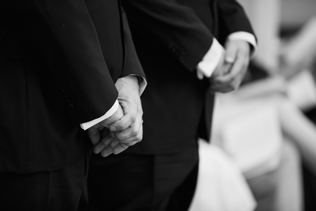 Black and white close-up of the two grooms holding hands