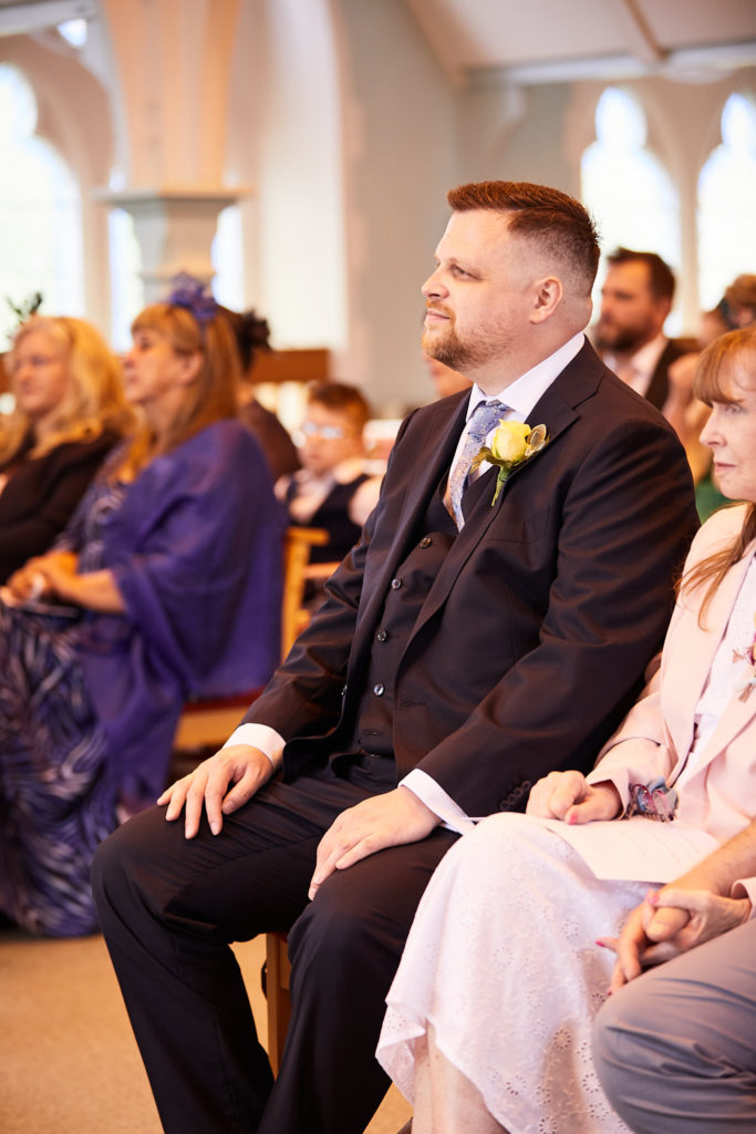Groom smiling as he sits among guests in the church