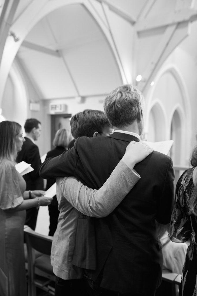 Black and white photo of a groom hugging a guest after the ceremony