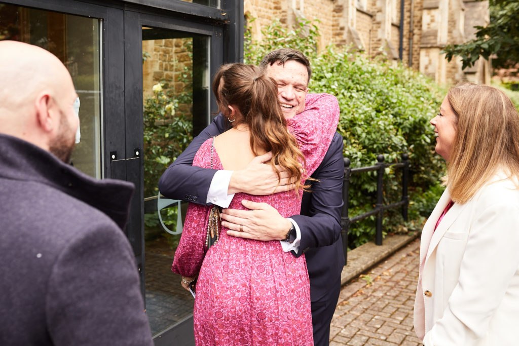 Groom hugging a guest in a pink dress outside the church