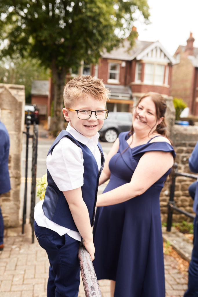 Young page boy in a waistcoat and glasses smiling beside a woman in a navy dress