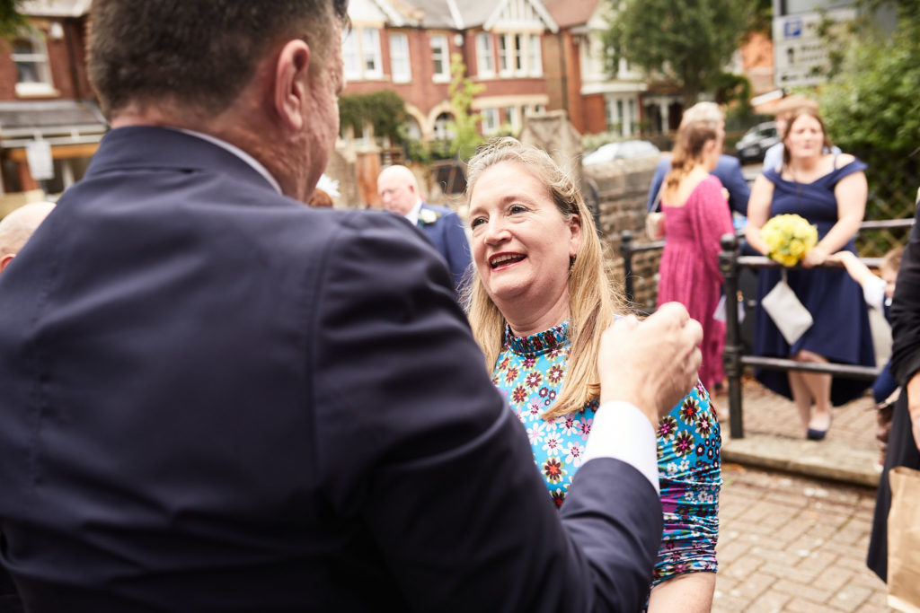Wedding guest laughing as she greets one of the grooms