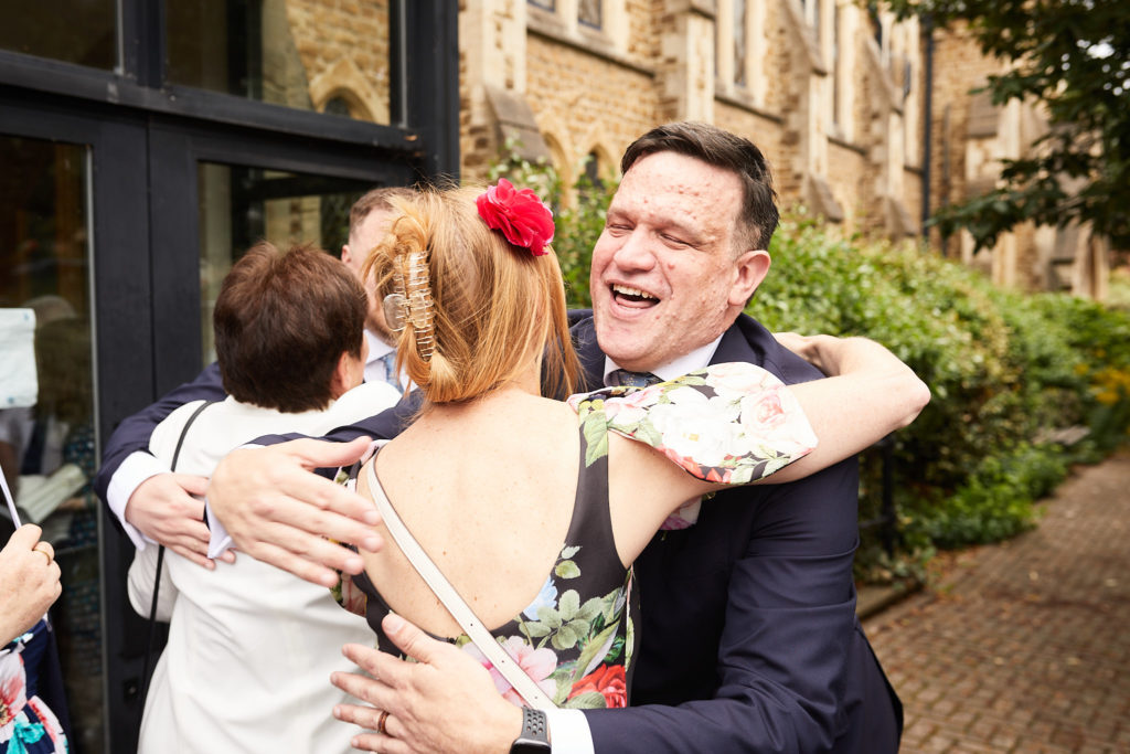 Groom laughing as he hugs a guest outside the church