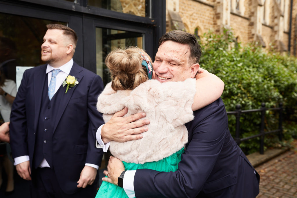 Groom hugging a guest as his husband looks on