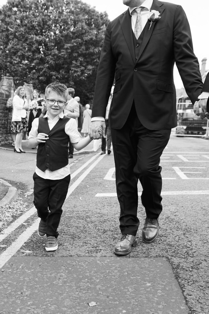 Black and white photo of a young page boy walking along the road beside a groom