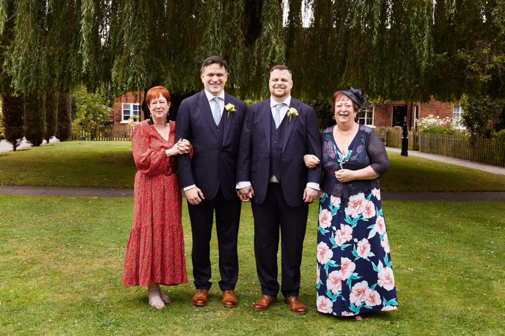 Two grooms with two women in floral dresses under a willow tree