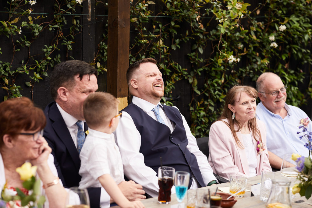 Two grooms laughing with their guests during the wedding breakfast