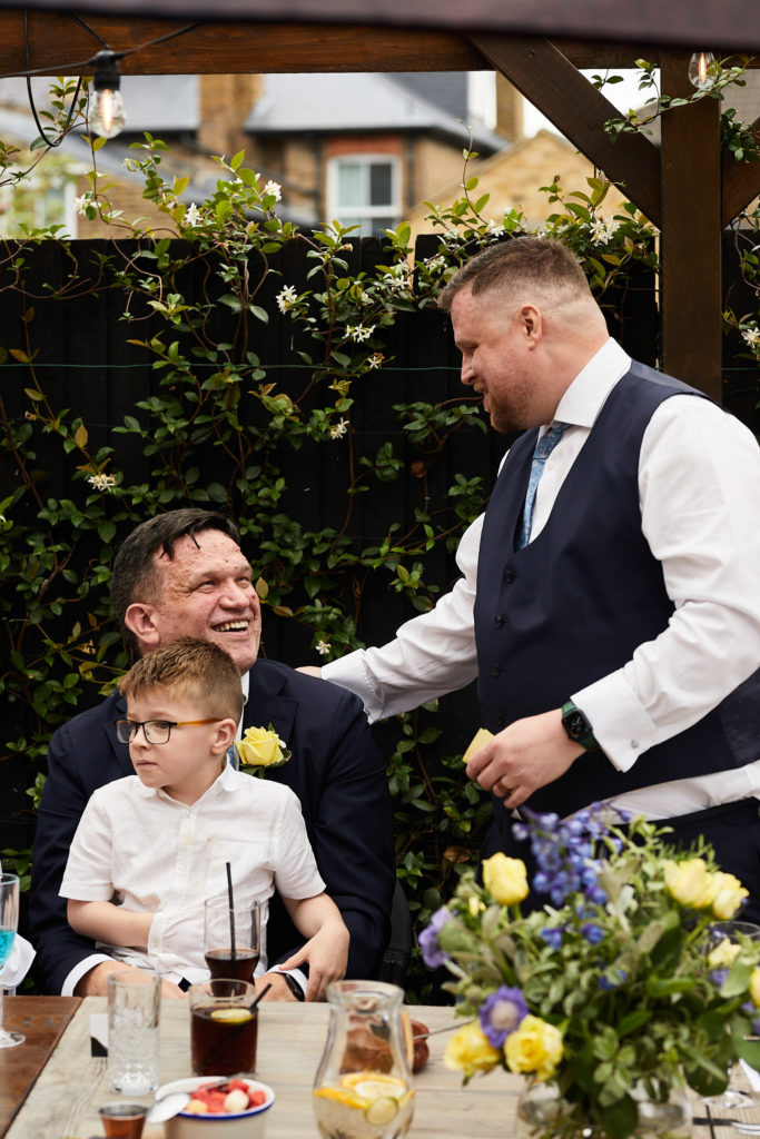 Groom standing behind his husband and a young page boy at the table