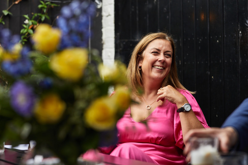 Wedding guest in a pink dress laughing, with yellow flowers in the foreground