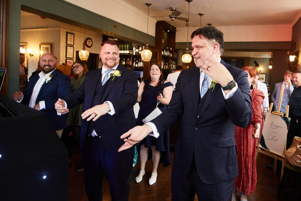 Two grooms dancing into the room as guests cheer