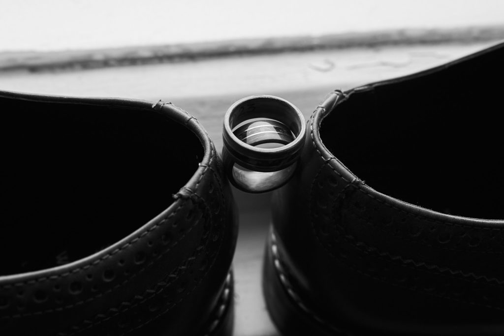 Black and white photo of wedding rings balanced between a pair of polished shoes