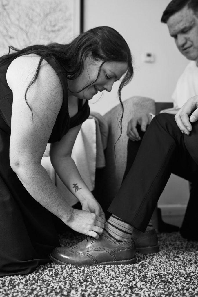 Black and white photo of the best woman tying a groom's shoelace