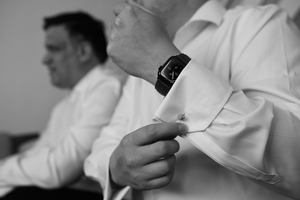 Black and white photo of a groom fastening his shirt cuff
