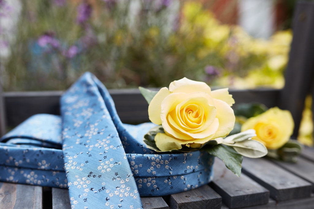 Pale blue tie and yellow rose buttonholes on a wooden table