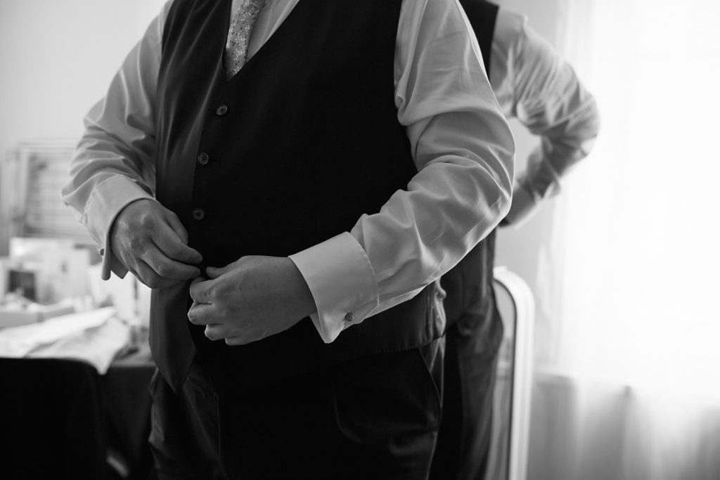 Black and white photo of a groom buttoning his waistcoat