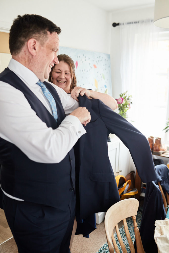 Groom being helped into his navy jacket by his best woman