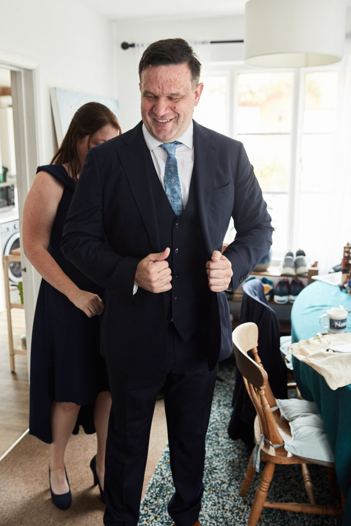 Groom laughing as he straightens his jacket with his best woman behind him