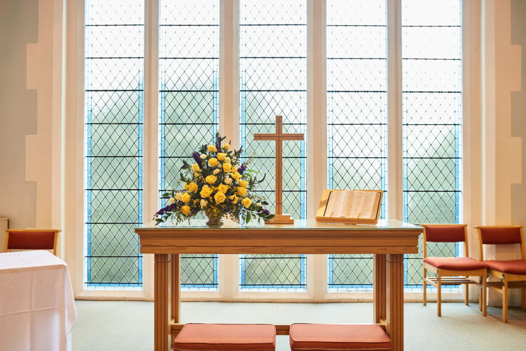 Altar table with a wooden cross and yellow flowers in front of a leaded window
