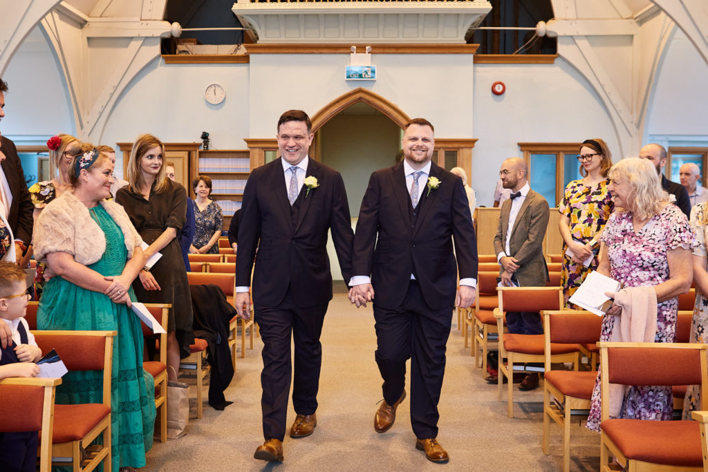 Two grooms walking down the aisle hand in hand at their LGBT church wedding