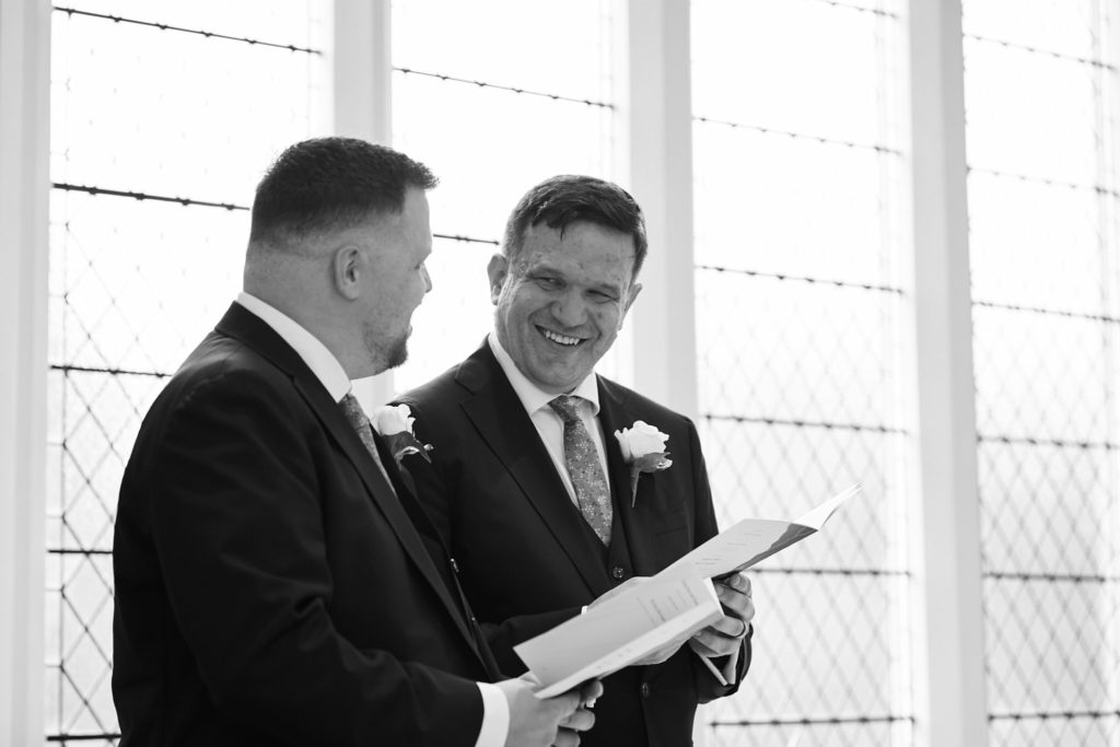 Black and white photo of the two grooms laughing as they read their vows