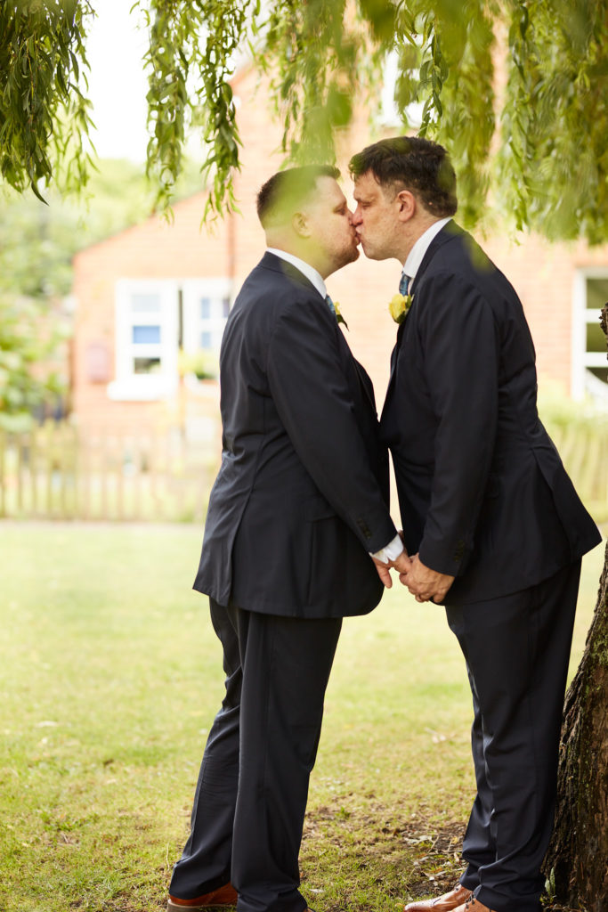 Two grooms kissing under a willow tree on their LGBT wedding day in Windsor, Berkshire