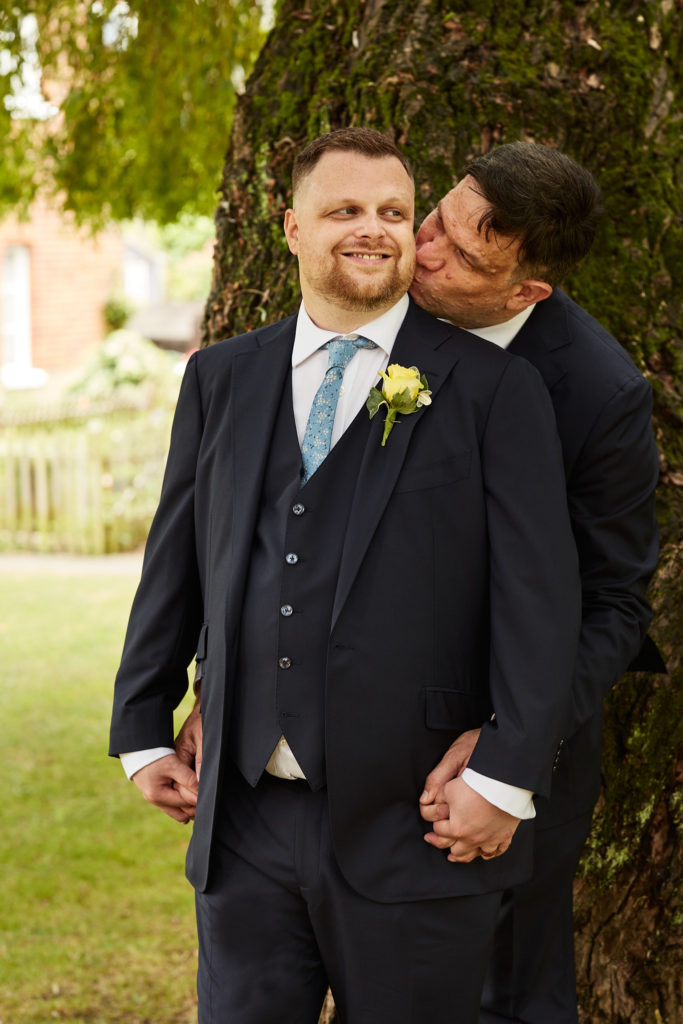 Groom kissing his husband on the cheek under a willow tree