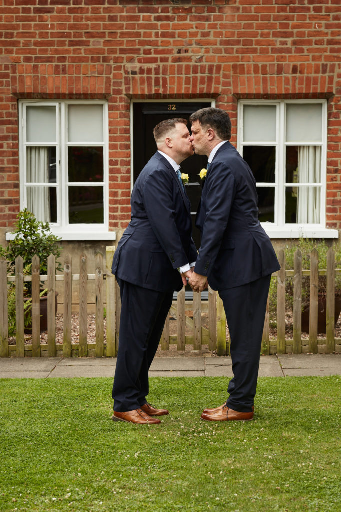 Newlywed grooms kissing in front of a red-brick cottage on their gay wedding day in Windsor