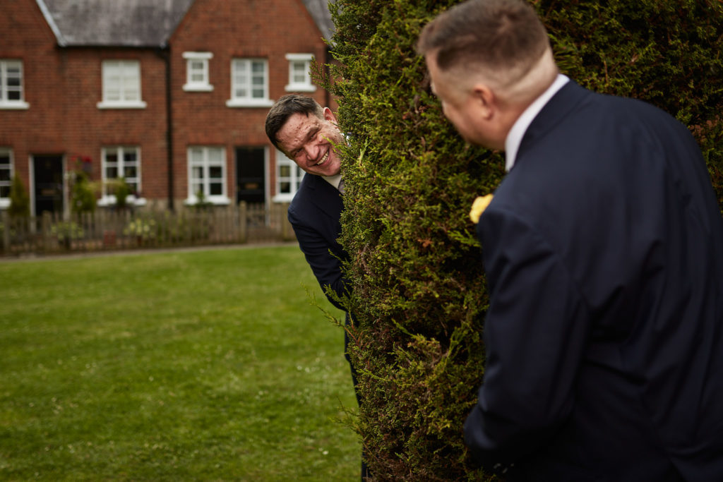 Groom peeking round a tree at his husband