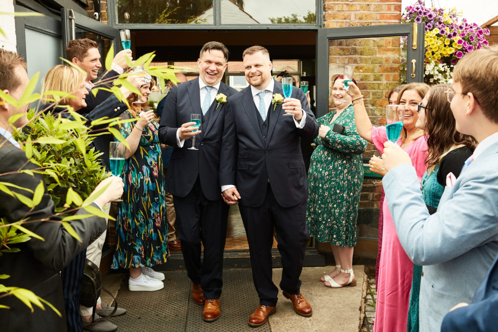 Two grooms arriving at their reception as guests applaud