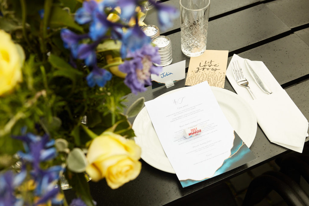 Place setting with a menu card beside blue and yellow flowers