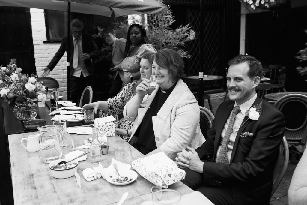 Black and white photo of a groom smiling at the table with guests